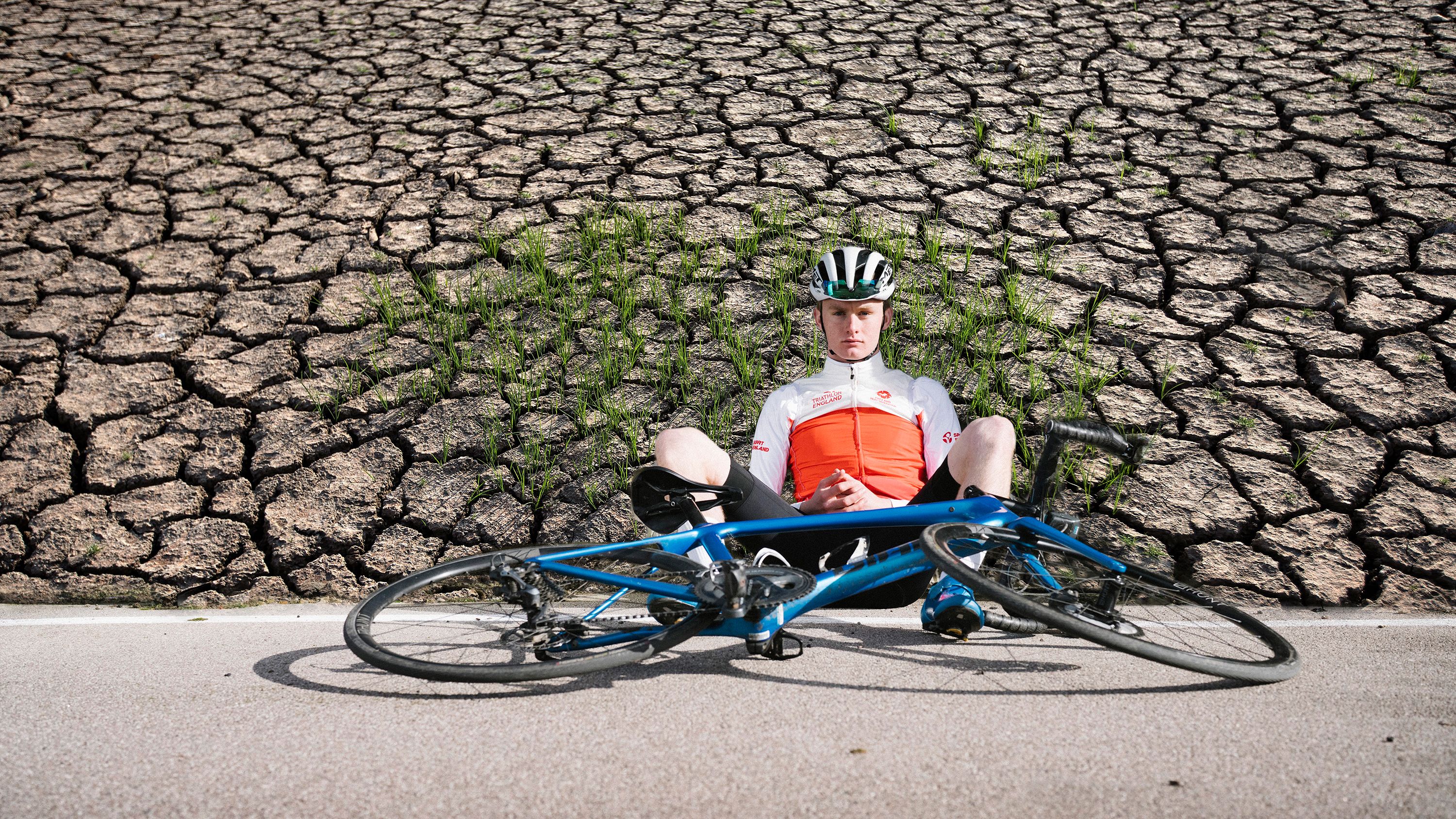 Young cyclist sits against dry, drought background