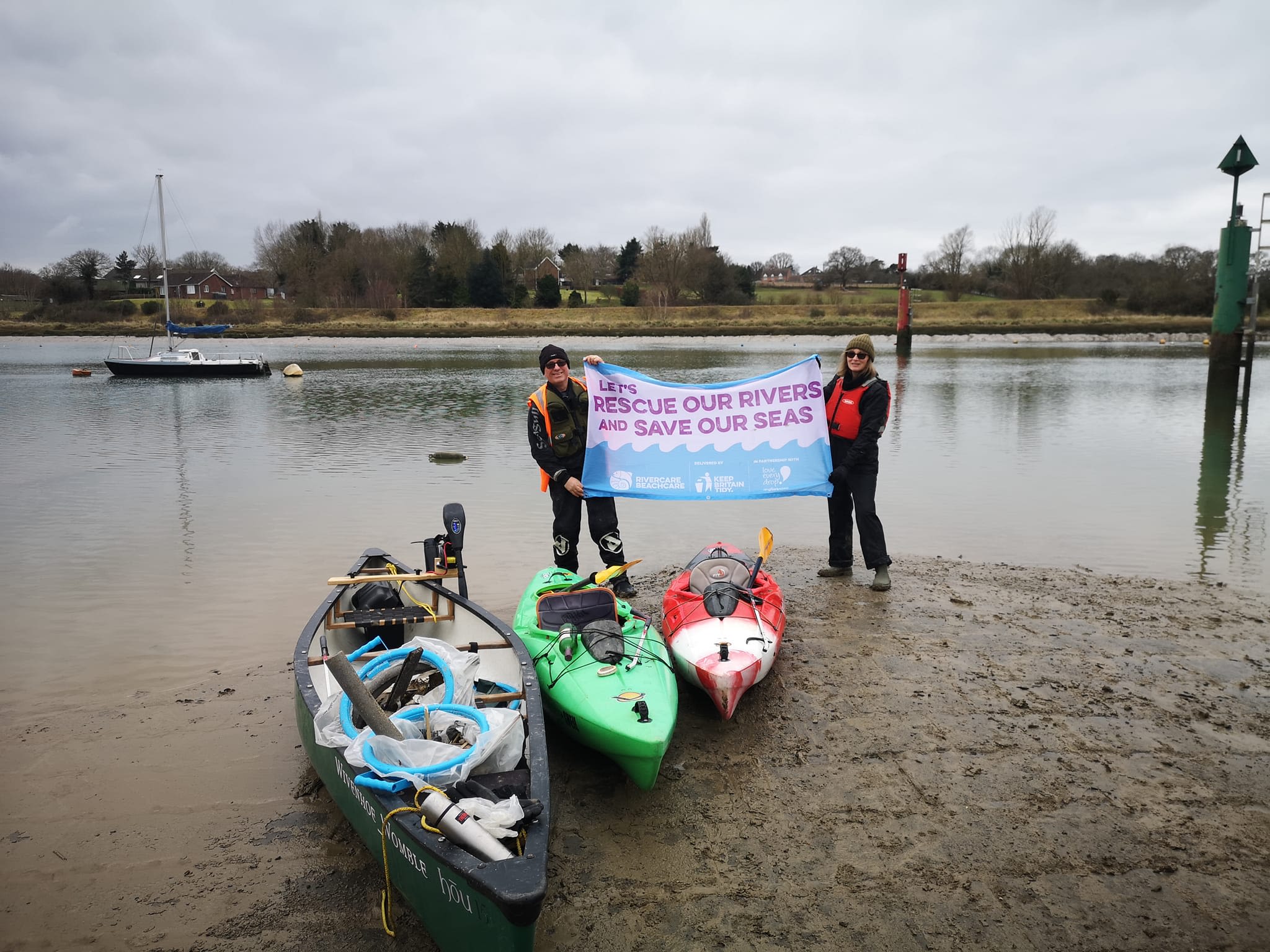 Two people holding an environmental sign by some canoes