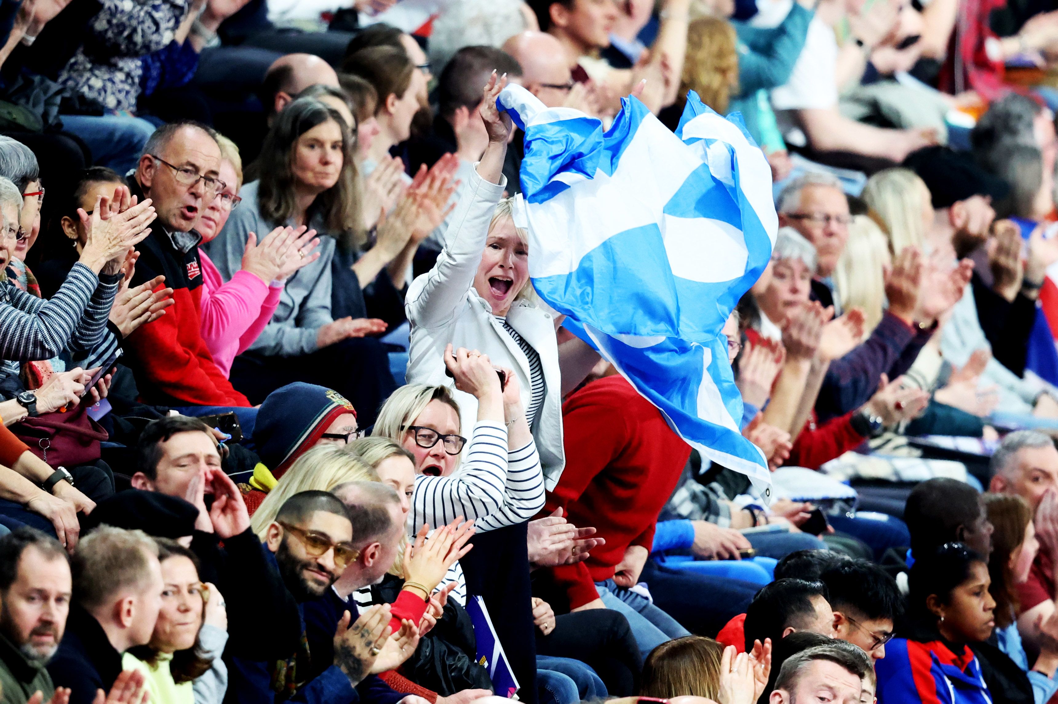 A women in the middle of shot waves a Scottish flag, surrounded by other cheering fans at the 2024 World Indoor Athletics Championships.
