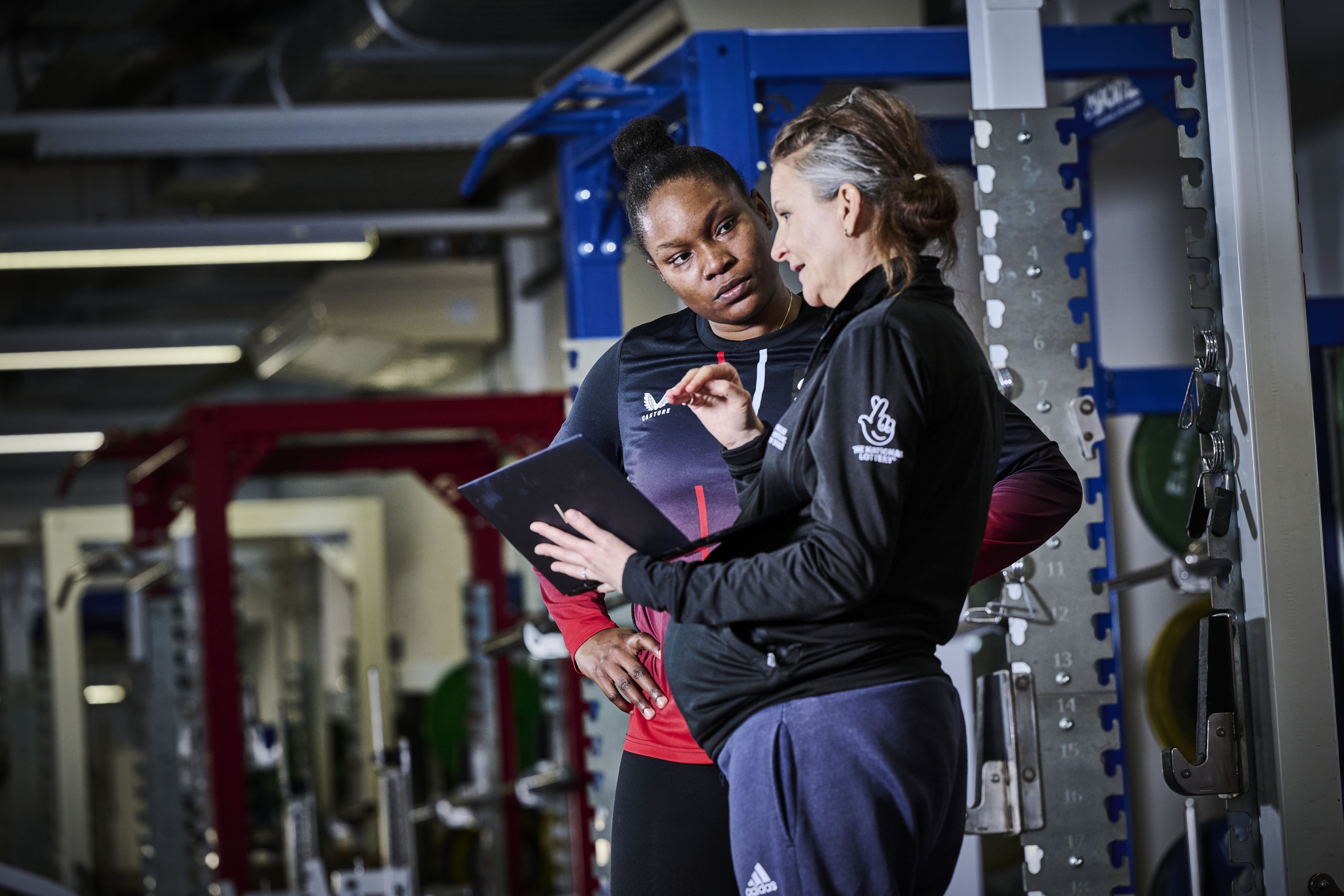 Two UKSI practitioners in conversation in a free weights gym.